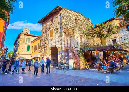 SIRMIONE, ITALIEN - 10. APRIL 2022: Fassade eines alten Steinhauses mit kleinen Restaurants im Freien an der Wand, Piazza Flaminia, am 10. April in Sirmione Stockfoto