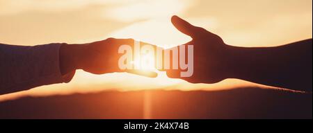 Eine helfende Hand geben. Rettung, helfende Geste oder Hände. Zwei Hände Silhouette auf Himmel Hintergrund, Verbindung oder Hilfe-Konzept Stockfoto