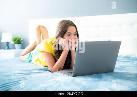 Teenager Kind Mädchen arbeiten auf Laptop-pc-Computer im Bett liegend entspannen im Schlafzimmer zu Hause. Teen Mädchen, positive und lächelnde Emotionen. Stockfoto