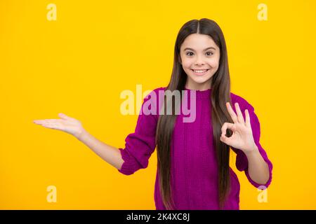 Positive Teenager Kind zeigt sich mit fröhlichem Ausdruck beiseite, zeigt erstaunlich auf leeren leeren Raum. Werbung und Mockup. Stockfoto