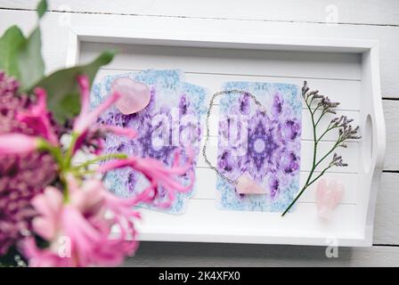 Deck mit hausgemachten Engelskarten auf weißem Tablett am heimischen Tisch, umgeben von Halbedelsteinen, Rosenquarzkristallen und engelförmiger Figur. Stockfoto