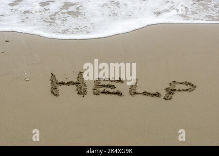 Worte in den Sand geschrieben. Das Wort HILFE im Sand mit dem Ozean im Hintergrund geschrieben. Stockfoto