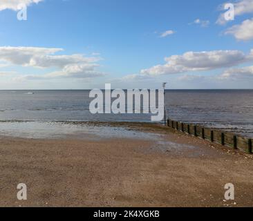 Wellenbrecher, der an einem Tag mit blauem Himmel über den Sandstrand hinaus ins Meer führt Stockfoto