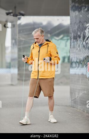 Vertikales Porträt eines hübschen reifen Mannes, der im Freien mit Springseil in einer städtischen Umgebung trainiert Stockfoto
