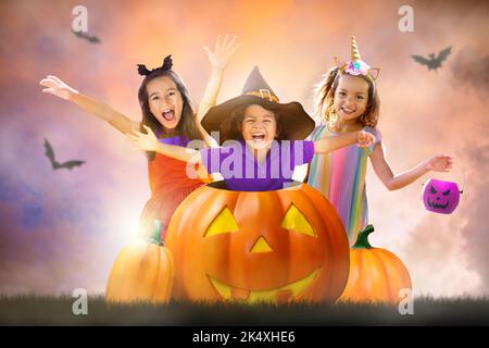 Kinder an der Halloween-Nacht. Kinder tricksen oder verwöhnen. Multiethnische Gruppe von Kindern in einer riesigen Kürbislaterne. Junge und Mädchen im Hexenkostüm Stockfoto