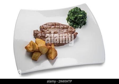 Gegrilltes Rinderfilet-Steak mit Spinat und gebackenen Kartoffeln auf weißem Teller, isoliert auf Weiß Stockfoto