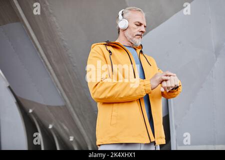 Porträt eines stattlichen älteren Mannes, der im Freien Kopfhörer trägt, vor einem Betonhintergrund in einer städtischen Umgebung, in einem Kopierraum Stockfoto