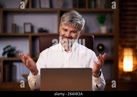 Porträt eines Geschäftsmanns im Büro, der lächelt und die Kamera anschaut. Erfolgreicher europäischer Mann in weißem Hemd, der am Schreibtisch sitzt und hat Stockfoto