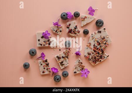 Handgemachte rosa Schokolade mit Beeren und Blumen. Gebrochene Riegel mit Haselnüssen, Mandeln und Himbeeren Stockfoto