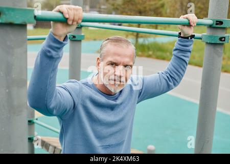 Porträt eines aktiven, reifen Mannes, der im Freien arbeitet und die Kamera in einer minimalistischen Stadtumgebung anschaut Stockfoto