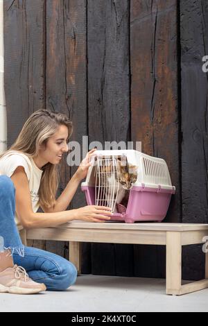 Vertikale Ansicht einer jungen lächelnden Frau, die die Hauskatze in einem Träger vom Tierarzt zurückbringt und das Haustier nach draußen kommt Stockfoto