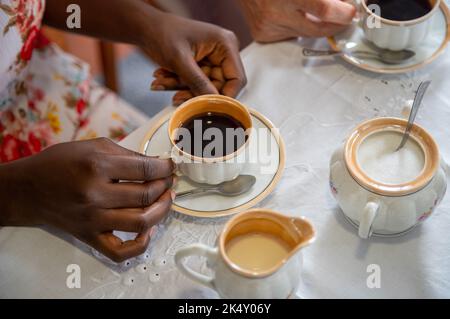 Junge Frau hält Hände mit einer alten Kaffeetasse. Interracial paar trinken schwarzen Kaffee. Mit Porzellankaffeeset Stockfoto