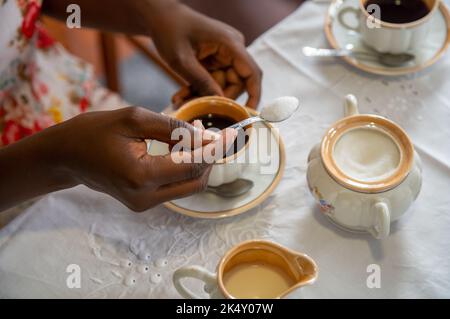 Junge Frau, die ihrem Kaffee Zucker zugab. Mit antikem Kaffeeset Stockfoto