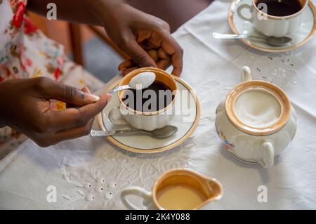 Junge Frau, die ihrem Kaffee Zucker zugab. Mit antikem Kaffeeset Stockfoto