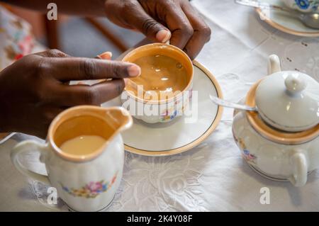 Junge Frau erstickt ihren weißen Kaffee. Mit antikem Kaffeeset Stockfoto