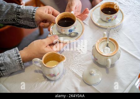 Junger Mann, der einer Dame eine Tasse Kaffee anbietet. Mit antikem Kaffeeset Stockfoto
