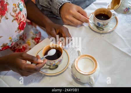 Junge Frau, die ihrem Kaffee Zucker zugab. Mit antikem Kaffeeset Stockfoto