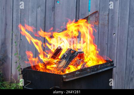 Brennende Kiefernstämme für Kohlen. Starke Flamme auf dem Grill. Brennendes Feuerholz auf dem Grill. Das Feuer brennt auf dem Grill. Stockfoto