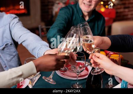 Verschiedene Menschen klirren Gläser mit Sekt aus der Nähe, schlagen Weihnachts-Toast, Alkohol zu trinken zum festlichen Abendessen. Weihnachtsfeier im Winter, Freunde treffen sich Stockfoto