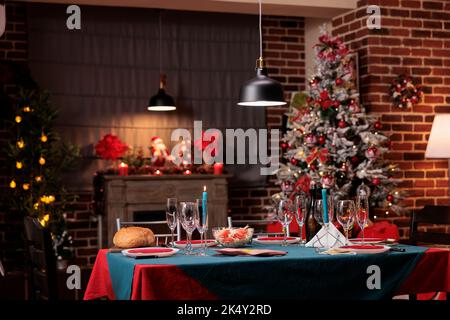 Weihnachtliche große Tischanordnung, wunderschön dekorierter Ort, warme Kerzenlichter in luxuriöser Innenausstattung. Winter Saisonferien traditionelle Zubereitungen, Weingläser, Geschirr auf der Tischplatte Stockfoto