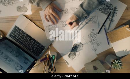Junge Illustratorin zeichnet Bleistiftskizzen auf Papier. Zeichnungen auf dem Blatt mit Papieren vor ihr. Illustration Animation, Storyboard, Videospiel Filmproduktion, Animation Design Studio. Stockfoto