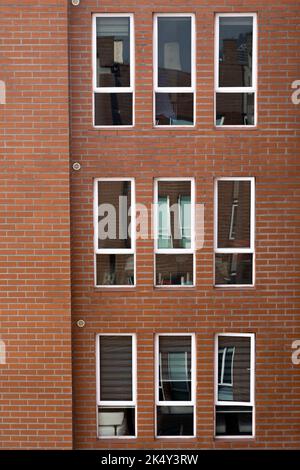 Wohnwohnung mit Fenstern und Backsteinmauer, Hintergrund mit Details der Architektur Dekoration, Textur und geometrische Figuren an der Fassade Stockfoto