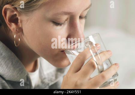 Das Mädchen trinkt Wasser aus einer transparenten Glasschale. Stockfoto