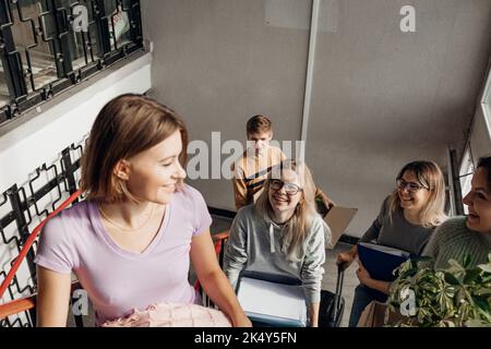 Lächelnd, froh, vorausahnend, die Schüler, die Gepäck und Sachen auf Treppen tragen, scherzen, während die Passage verlegt wird Stockfoto