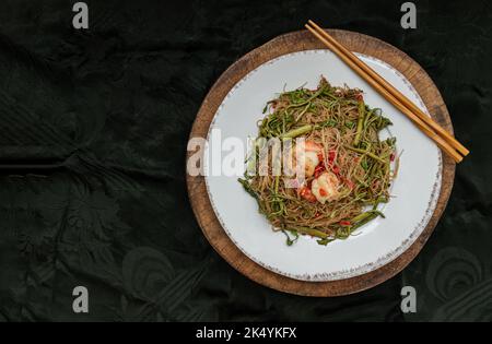 Gebratener Reis vermicelli & Wasser Mimosa mit Garnelen auf weißem Keramikplatte serviert mit hölzernen Essstäbchen mit dunklem Hintergrund. Thailändische Küche, Top vie Stockfoto