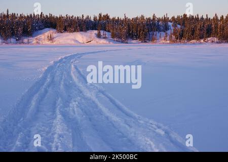 Sonnenaufgang am Frame Lake in Yellowknife, Kanada, gekennzeichnet durch die Spuren von Menschen, die Wintersport in der gefrorenen Umgebung genießen. Stockfoto