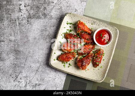 Honey Glazed Chicken Wings mit Tomatensauce auf einem quadratischen Teller auf dunklem Hintergrund. Draufsicht, flach liegend Stockfoto
