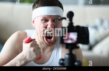 Porträt eines schreienden Bloggers, der Hanteln vor der Kamera hält Stockfoto