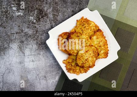 Rustikale hausgemachte Zucchini-Pfannkuchen auf einem weißen quadratischen Teller auf dunklem Hintergrund. Draufsicht, flach liegend Stockfoto