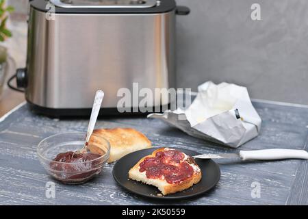 Toast mit Butter und Beerenmarmelade auf einem Holztisch neben dem Toaster. Frühstückszeit Stockfoto