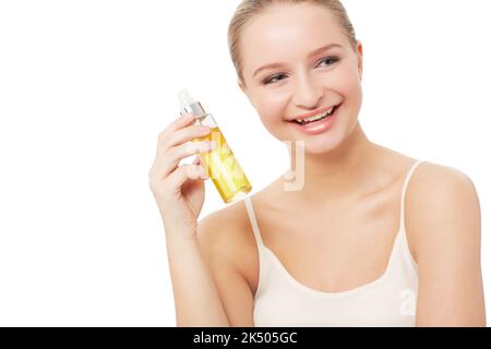 Zufrieden mit ihren Beauty-Produkten. Eine hübsche junge Frau, die eine Flasche Parfüm in der Hand hält, während sie auf weißem Hintergrund isoliert ist. Stockfoto