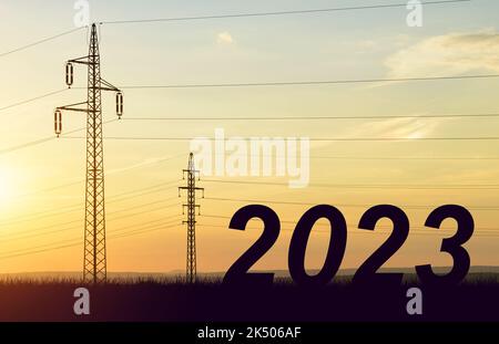 Die Zahl 2023 mit elektrischen Pylonen bei Sonnenuntergang. Konzept der hohen Preis für Strom oder Frohes neues Jahr. Stockfoto