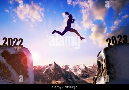 Silhouette das Mädchen springt bei Sonnenuntergang ins neue Jahr 2023. Stockfoto
