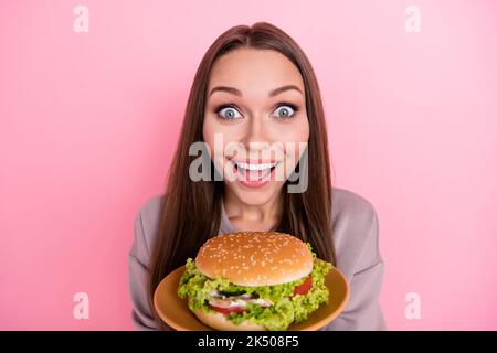 Porträt der staunenden fröhlichen Dame toothy Lächeln Hände halten Burger Teller isoliert auf rosa Hintergrund Stockfoto