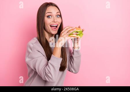 Portrait von funky positive Dame Hände halten Burger toothy Lächeln isoliert auf rosa Hintergrund Stockfoto