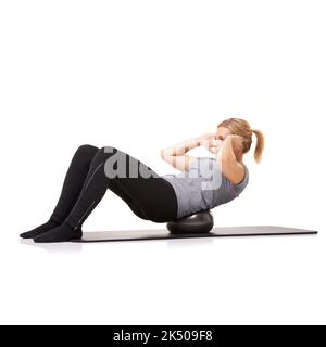 Crunches mit einem Gymnastikball. Eine junge Frau, die Sit-ups auf einem Übungsball macht, während sie auf weißem Hintergrund isoliert ist. Stockfoto