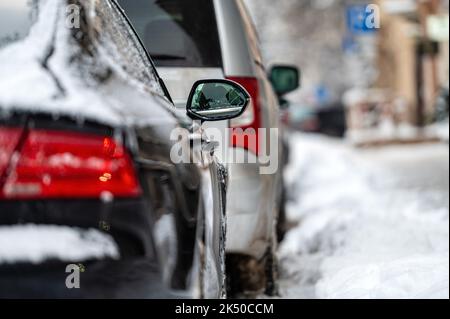 Autos auf verschneiten Straßen geparkt, Rückansicht, selektiver Fokus auf Rückspiegel Stockfoto