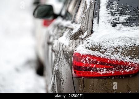 Autos, die auf verschneiten Straßen geparkt wurden, Seitenansicht hinten, selektiver Fokus auf die Heckleuchten Stockfoto