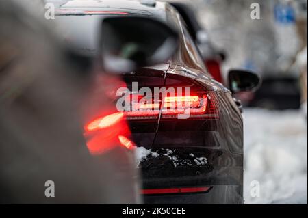 Autos, die auf verschneiten Straßen geparkt wurden, Seitenansicht hinten, selektiver Fokus auf die Heckleuchten Stockfoto