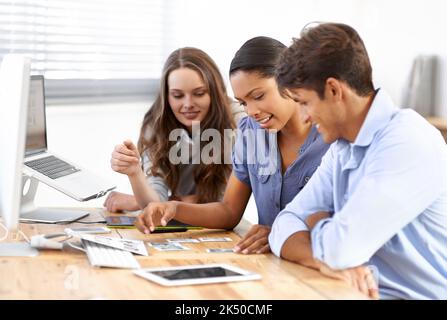 Die Wahl des richtigen Bildes, um die Marke zu bewerben. Drei junge Redakteure, die sich Fotos in ihrem Büro ansehen. Stockfoto