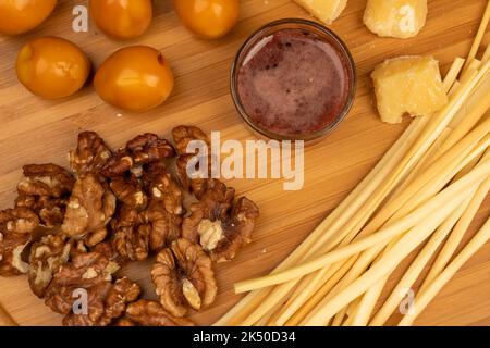 Verschiedene Sorten von Käse, Walnusskernen, geräucherten Wachteleiern und Honig in einer Glasvase auf einer Holzoberfläche. Stockfoto