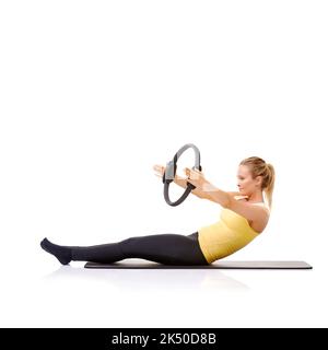 Der Pilates-Ring erfordert Gleichgewicht und Kraft. Eine hübsche junge Blondine, die die Roll-up-Übung mit ihrem Pilates-Ring durchführt. Stockfoto