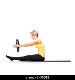 Straffung ihrer Kernmuskeln. Eine hübsche junge Blondine, die die Roll-up-Übung mit ihrem Pilates-Ring durchführt. Stockfoto
