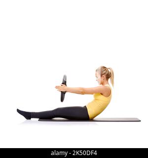 Sie kann spüren, wie sich ihre Bauchmuskeln anspannen. Eine hübsche junge Blondine, die die Roll-up-Übung mit ihrem Pilates-Ring durchführt. Stockfoto