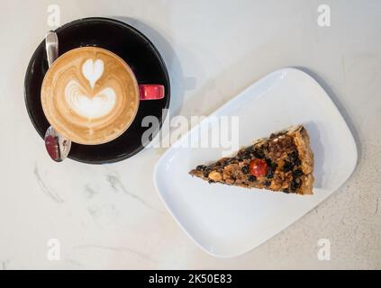 Eine Scheibe Ecclefechan Tart auf einem weißen Teller mit einer Tasse flachen weißen Kaffee Stockfoto