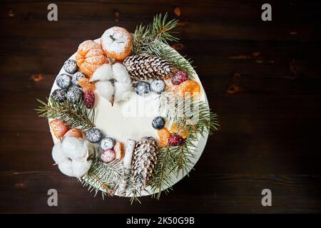 Weihnachtskuchen aus Schokoladenbasis mit Creme, verziert mit Beeren und Früchten auf Holzboden Stockfoto